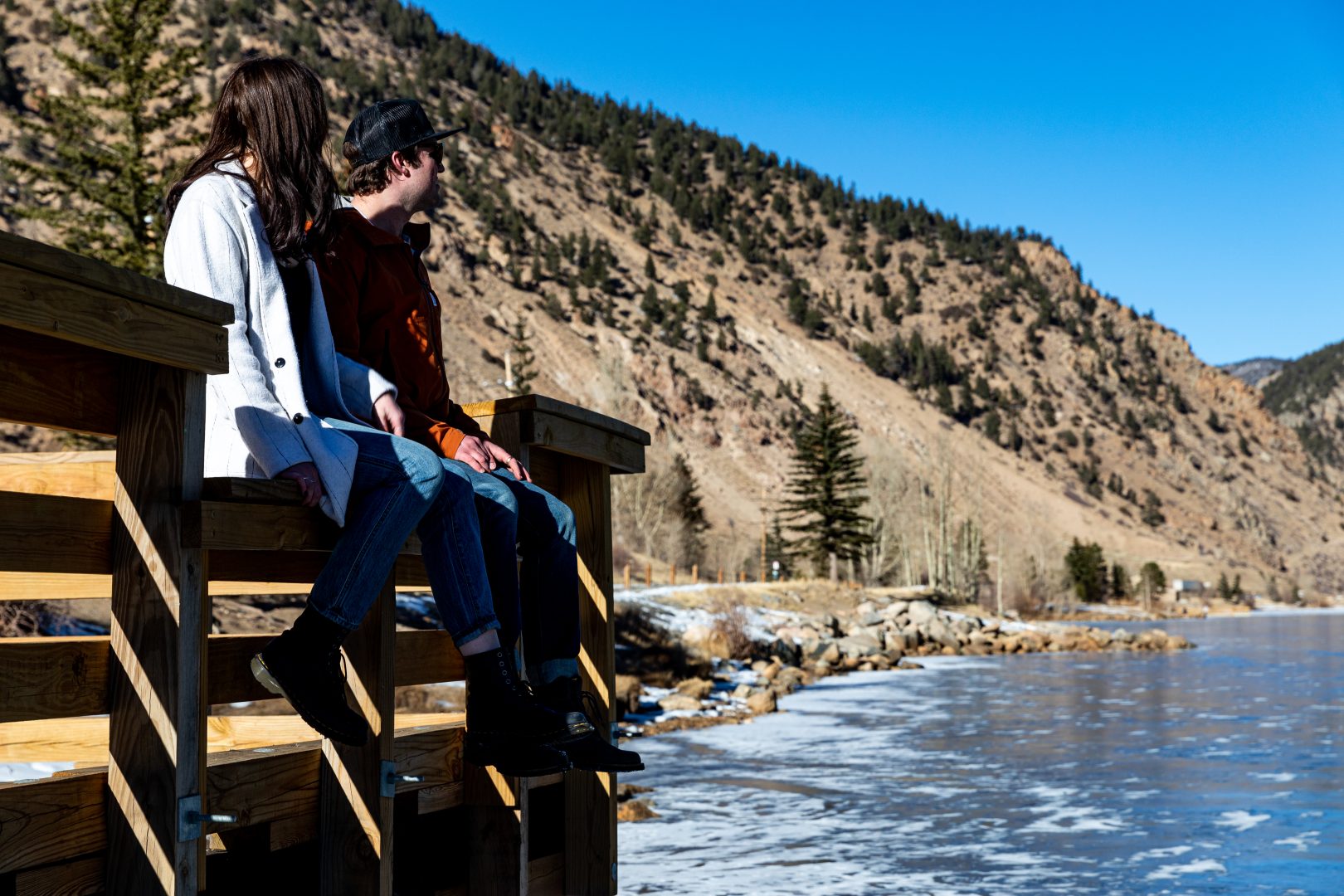 two people sitting on a wooden bench overlooking the water at The Bighorn Crossing
