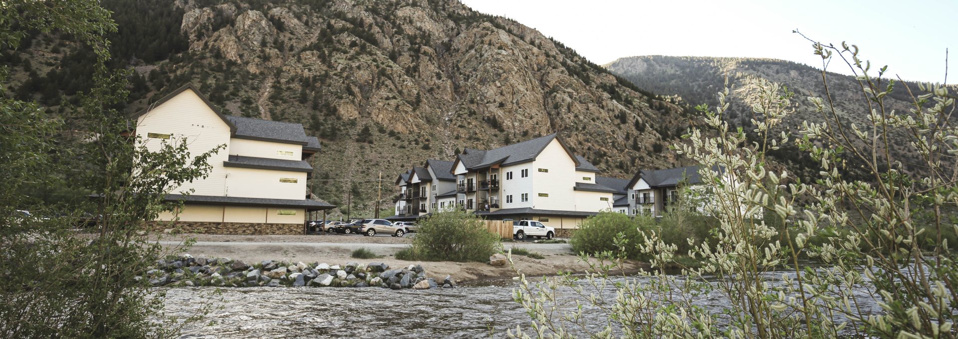 a river runs through a mountain range with houses on the banks at The Bighorn Crossing